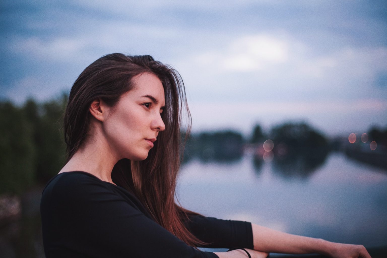 Photo d'une femme assise à côté d'un point d'eau et regardant devant elle.